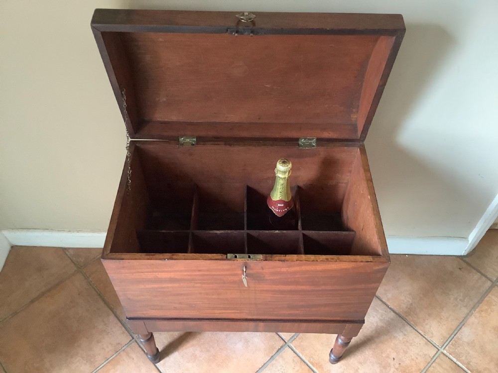 A Georgian mahogany cellarette featuring a domed lid, turned legs, flame mahogany wood grain, and side brass handles. View V