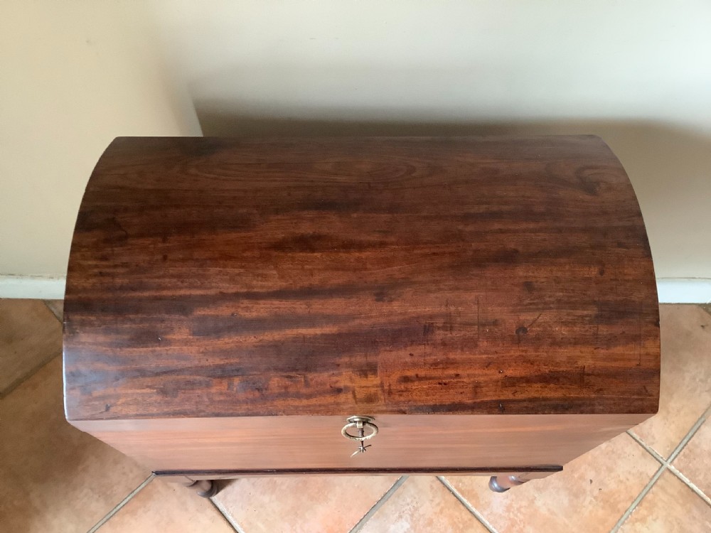 A Georgian mahogany cellarette featuring a domed lid, turned legs, flame mahogany wood grain, and side brass handles. View VI