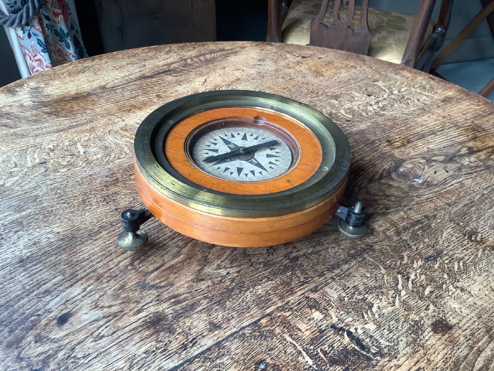 A circular antique brass and wood desk compass with adjustable levelling feet resting on a wooden surface.