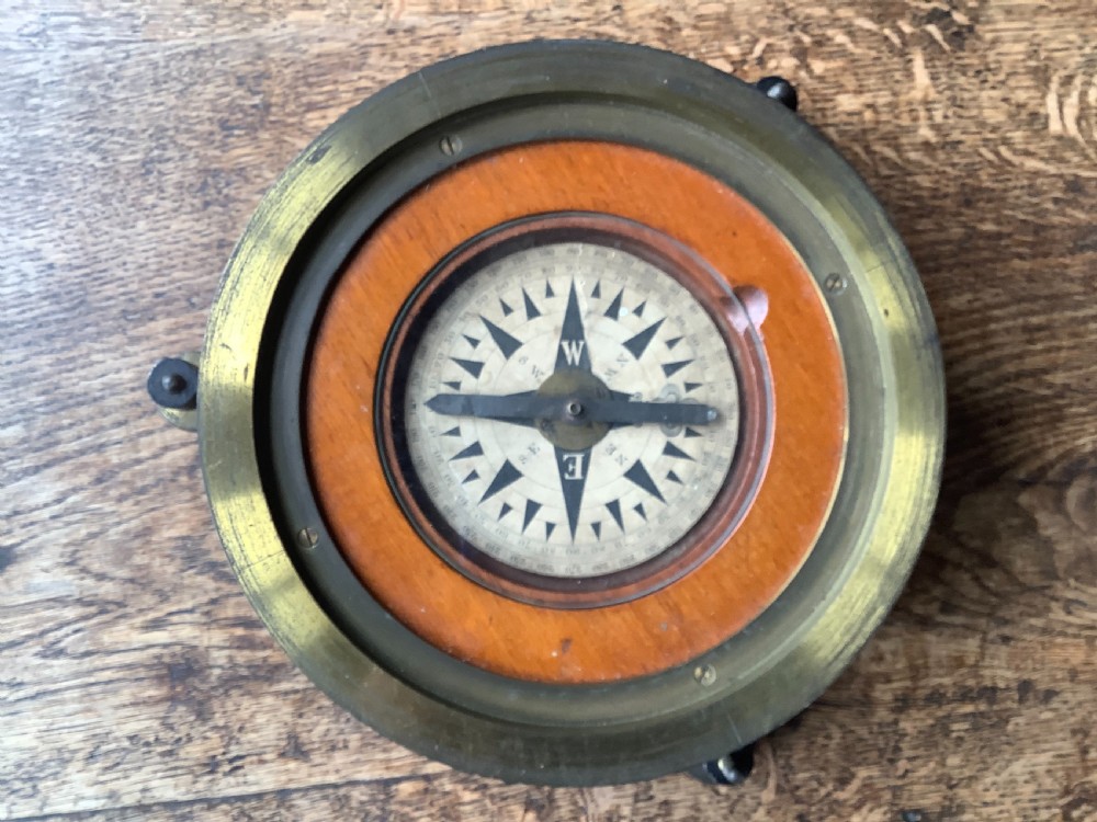 A circular antique brass and wood desk compass with adjustable levelling feet resting on a wooden surface. View III