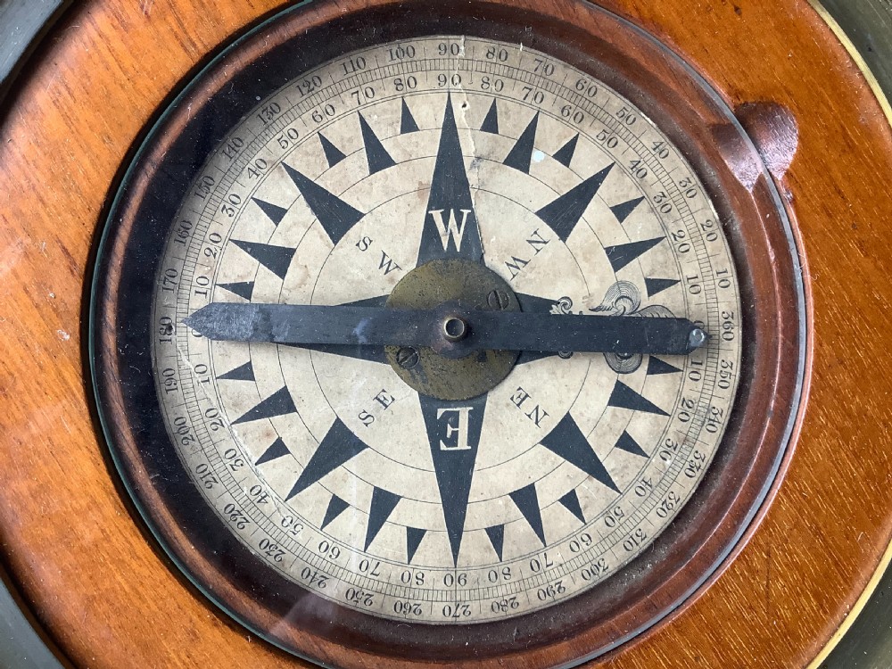 A circular antique brass and wood desk compass with adjustable levelling feet resting on a wooden surface. View V