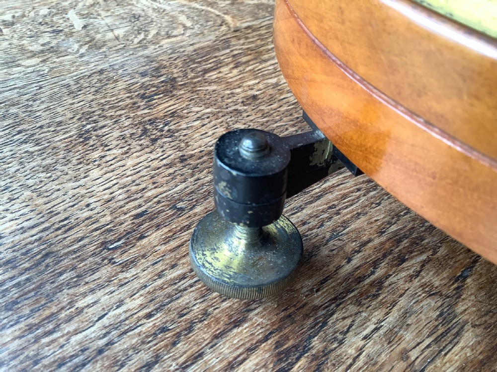 A circular antique brass and wood desk compass with adjustable levelling feet resting on a wooden surface. View VI
