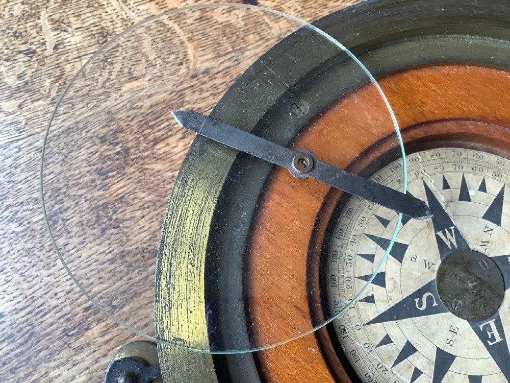 A circular antique brass and wood desk compass with adjustable levelling feet resting on a wooden surface. View VII
