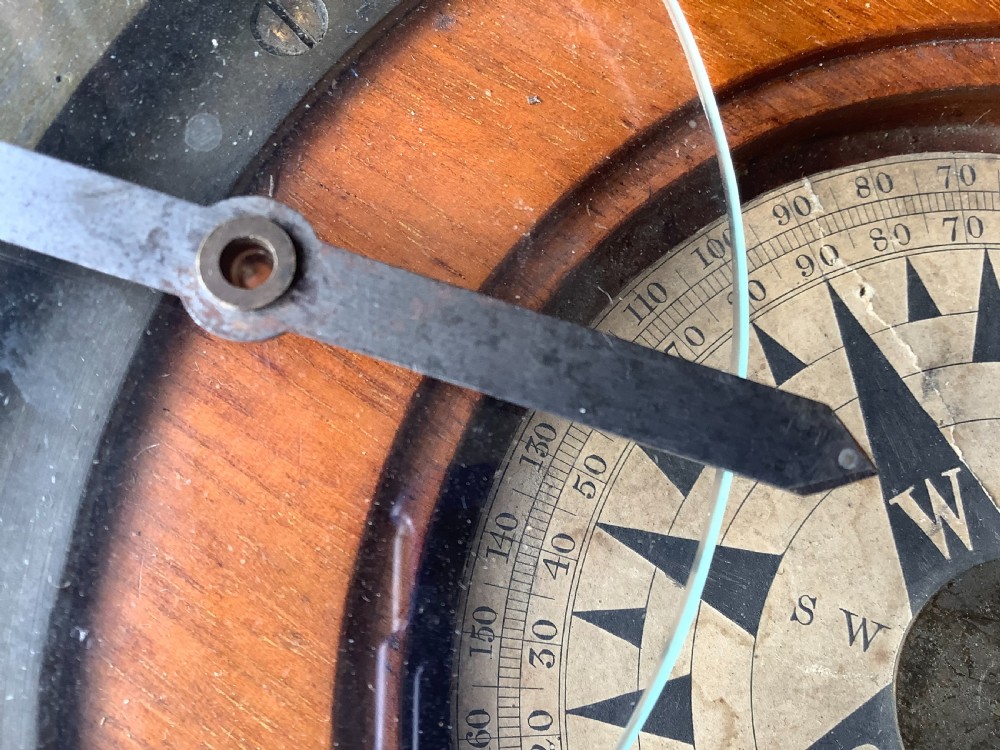 A circular antique brass and wood desk compass with adjustable levelling feet resting on a wooden surface. View VIII