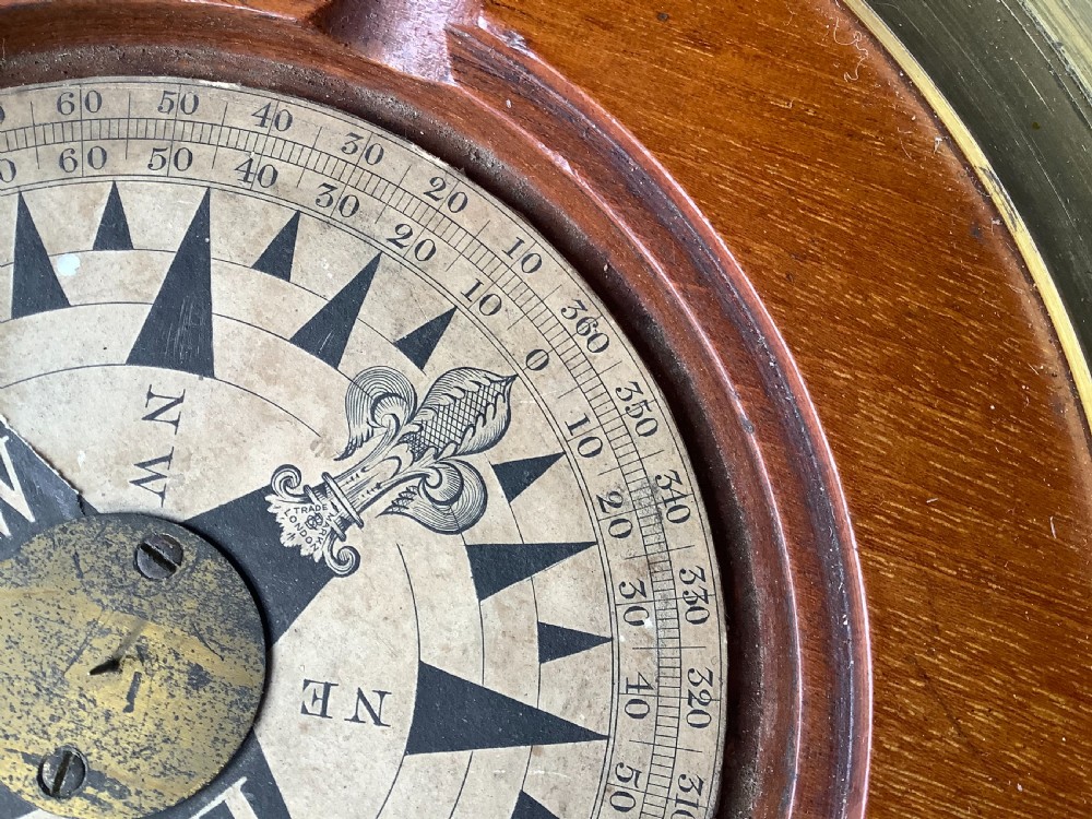 A circular antique brass and wood desk compass with adjustable levelling feet resting on a wooden surface. View IX