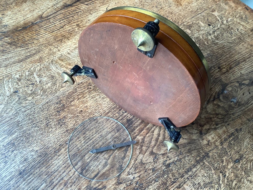A circular antique brass and wood desk compass with adjustable levelling feet resting on a wooden surface. View X