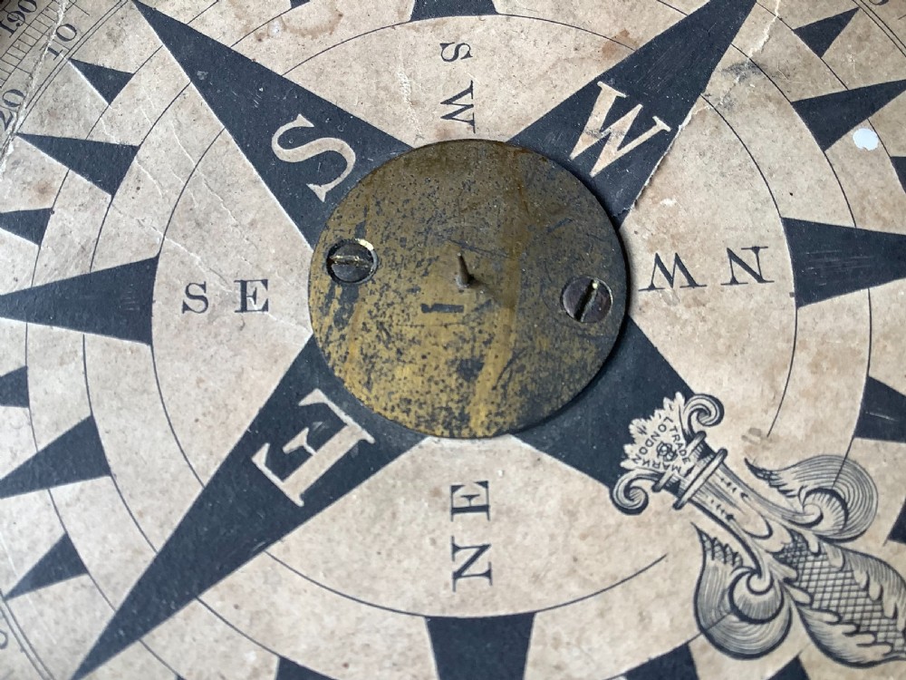 A circular antique brass and wood desk compass with adjustable levelling feet resting on a wooden surface. View XI