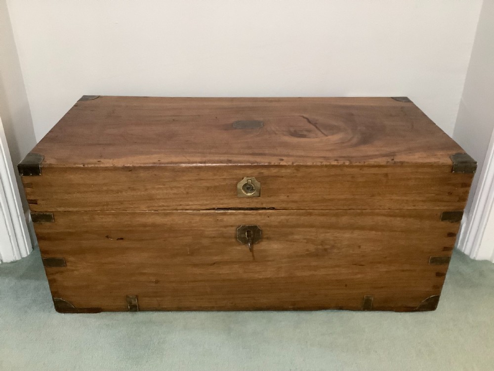 A rectangular camphor wood campaign trunk featuring flush brass corner brackets, central brass escutcheon, side carrying handles, and visible dovetail joinery.