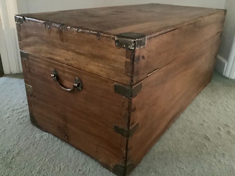 A rectangular camphor wood campaign trunk featuring flush brass corner brackets, central brass escutcheon, side carrying handles, and visible dovetail joinery. View X