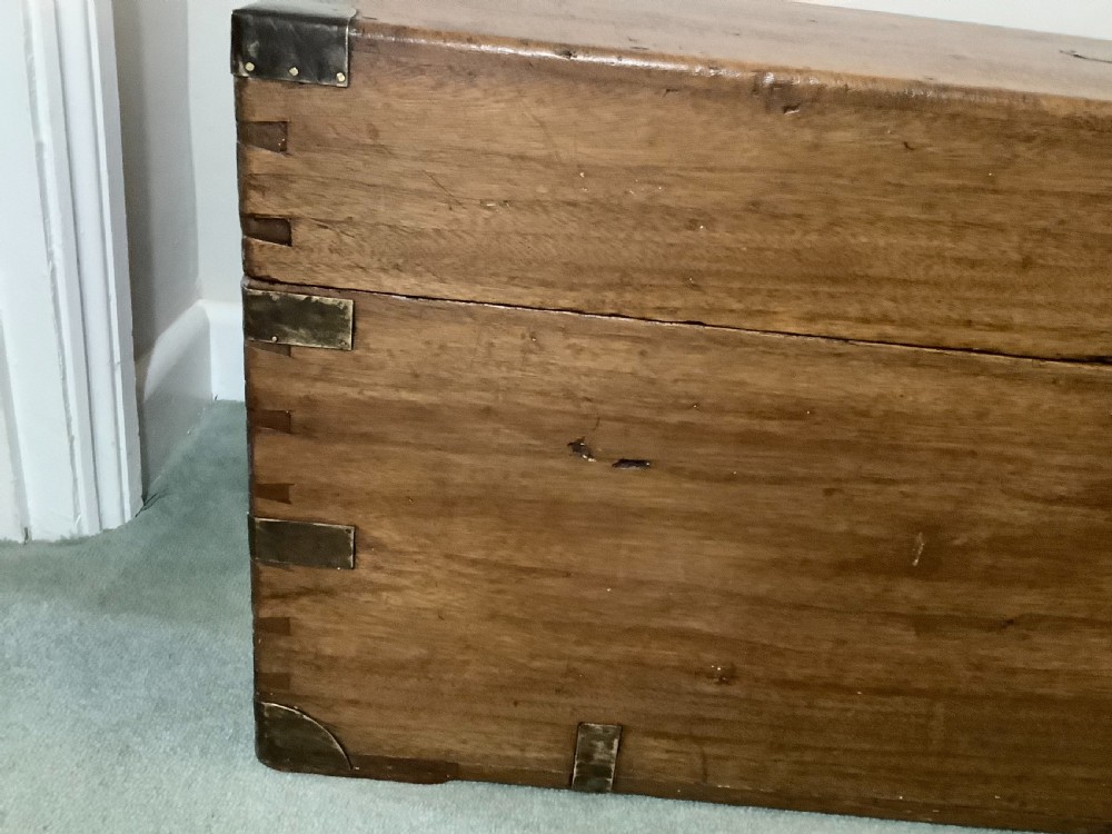 A rectangular camphor wood campaign trunk featuring flush brass corner brackets, central brass escutcheon, side carrying handles, and visible dovetail joinery. View XI