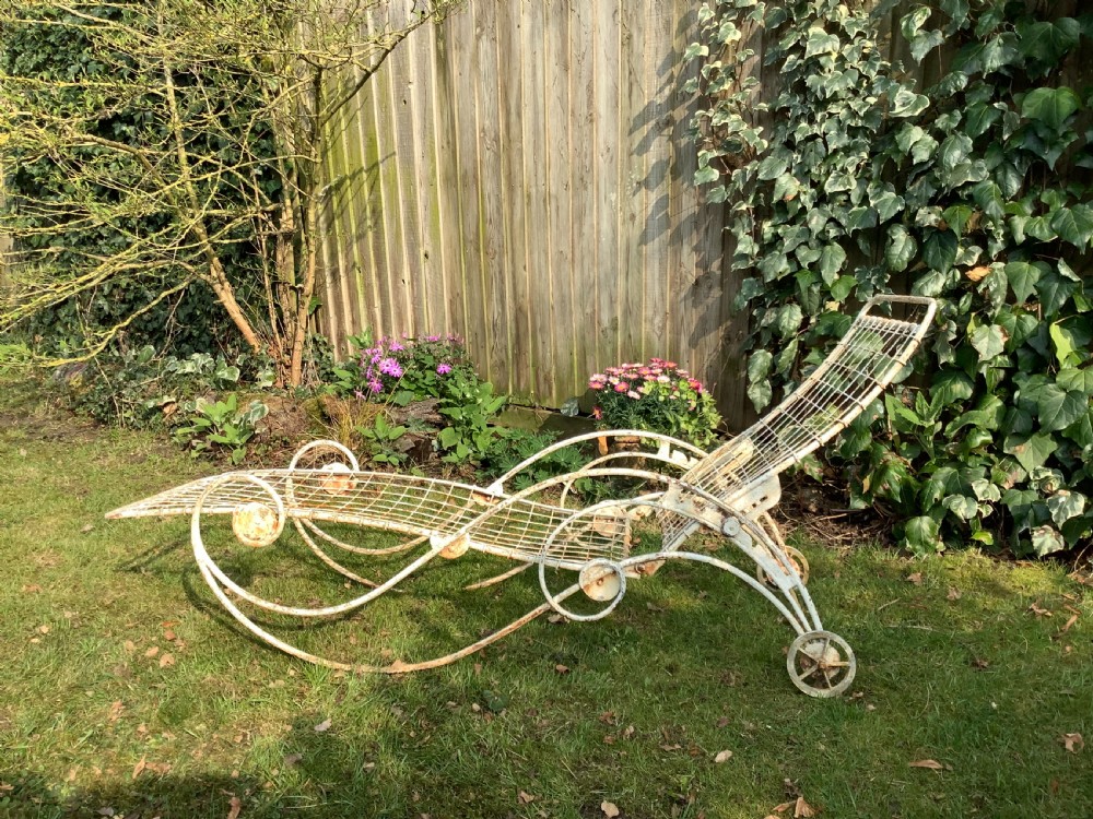 A weathered white wrought iron French garden lounger with a wire mesh reclining seat, curved scroll framework, and integrated wheels. View II