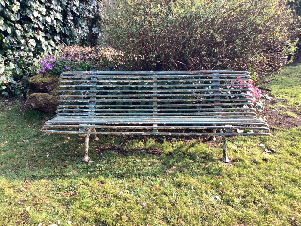 A weathered green iron Arras garden bench with horizontal slatted metal back and seat set on a lawn.