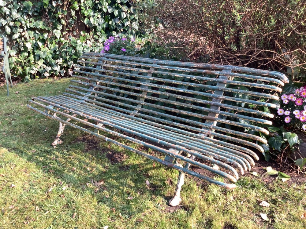 A weathered green iron Arras garden bench with horizontal slatted metal back and seat set on a lawn. View II