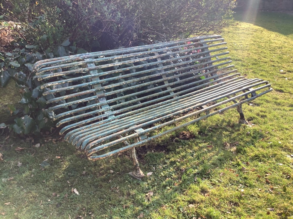 A weathered green iron Arras garden bench with horizontal slatted metal back and seat set on a lawn. View III