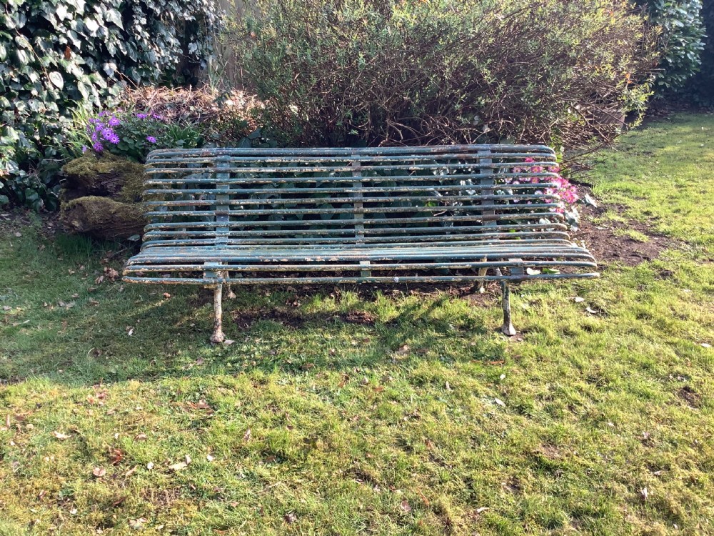 A weathered green iron Arras garden bench with horizontal slatted metal back and seat set on a lawn. View V