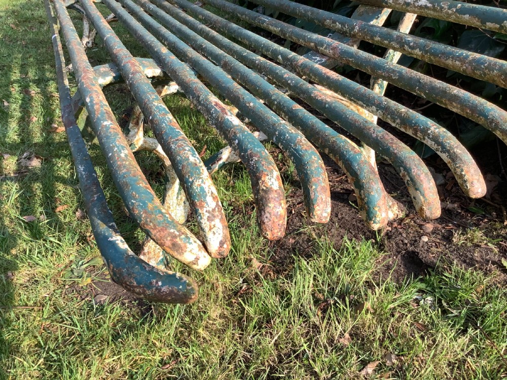 A weathered green iron Arras garden bench with horizontal slatted metal back and seat set on a lawn. View VII