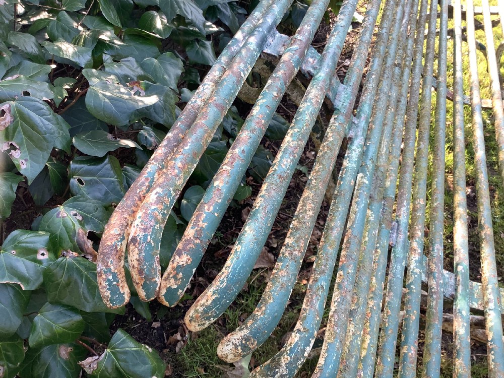 A weathered green iron Arras garden bench with horizontal slatted metal back and seat set on a lawn. View X