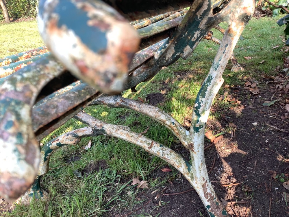 A weathered green iron Arras garden bench with horizontal slatted metal back and seat set on a lawn. View XII