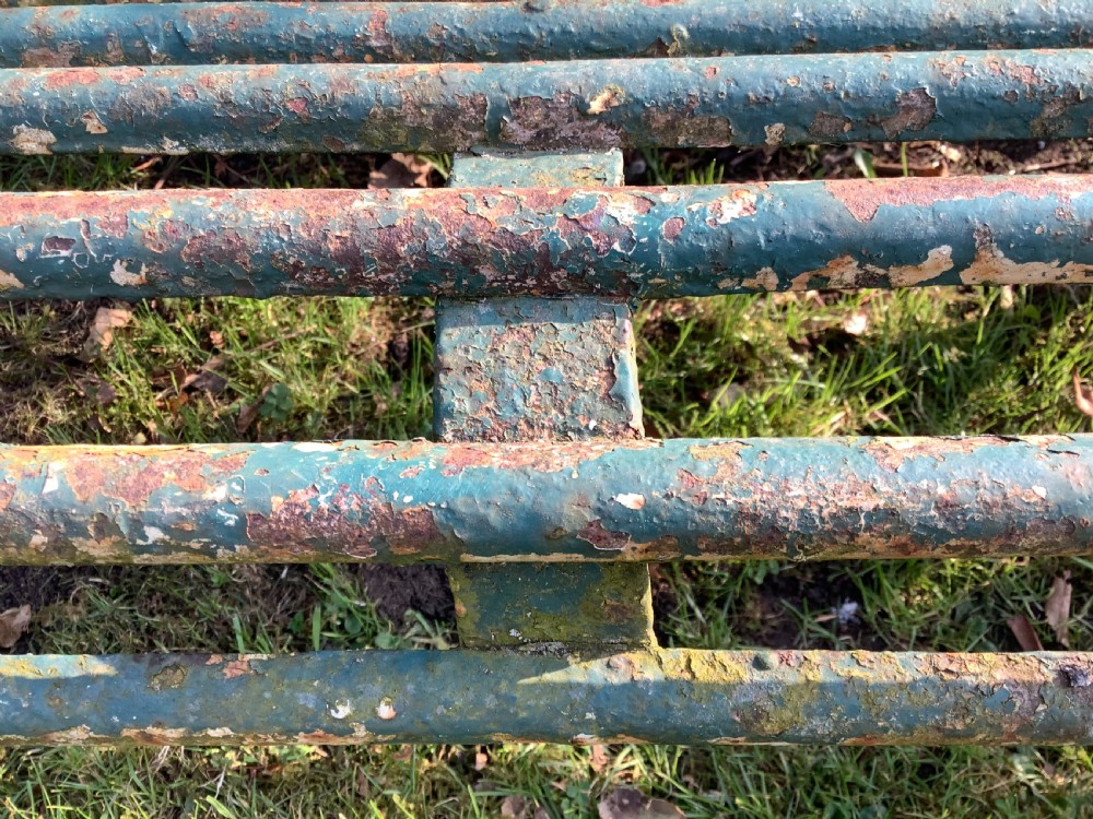 A weathered green iron Arras garden bench with horizontal slatted metal back and seat set on a lawn. View XIII