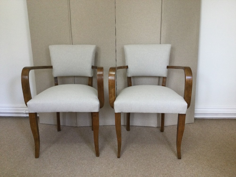 A pair of French Art Deco bridge chairs featuring curved wooden arms and light beige fabric upholstery.