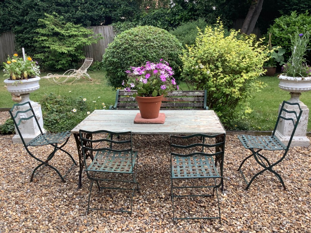 A set of four weathered green painted French folding iron garden chairs with lattice strap seats resting on grass. View II