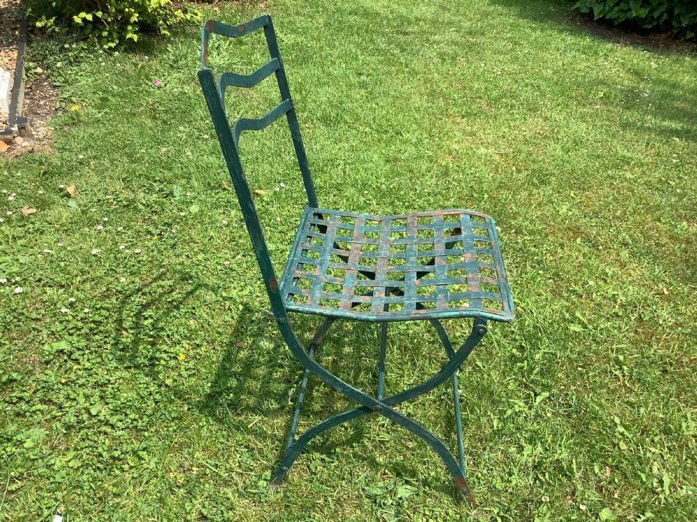 A set of four weathered green painted French folding iron garden chairs with lattice strap seats resting on grass. View V