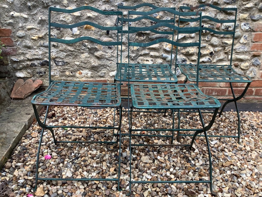 A set of four weathered green painted French folding iron garden chairs with lattice strap seats resting on grass. View VI
