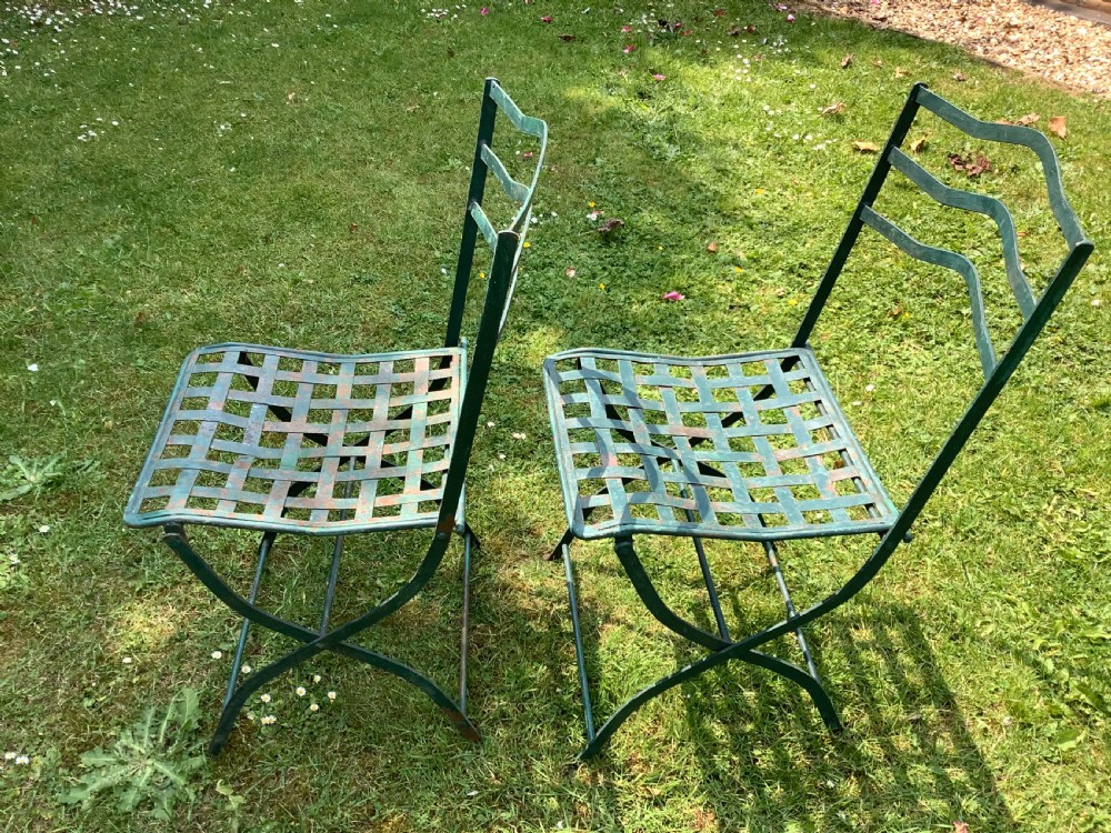 A set of four weathered green painted French folding iron garden chairs with lattice strap seats resting on grass. View VII