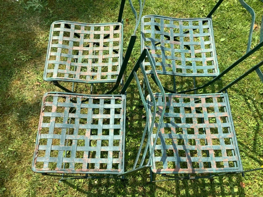 A set of four weathered green painted French folding iron garden chairs with lattice strap seats resting on grass. View VIII