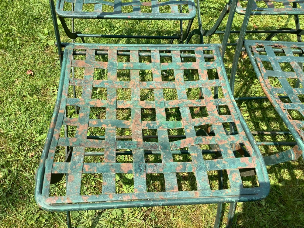 A set of four weathered green painted French folding iron garden chairs with lattice strap seats resting on grass. View X