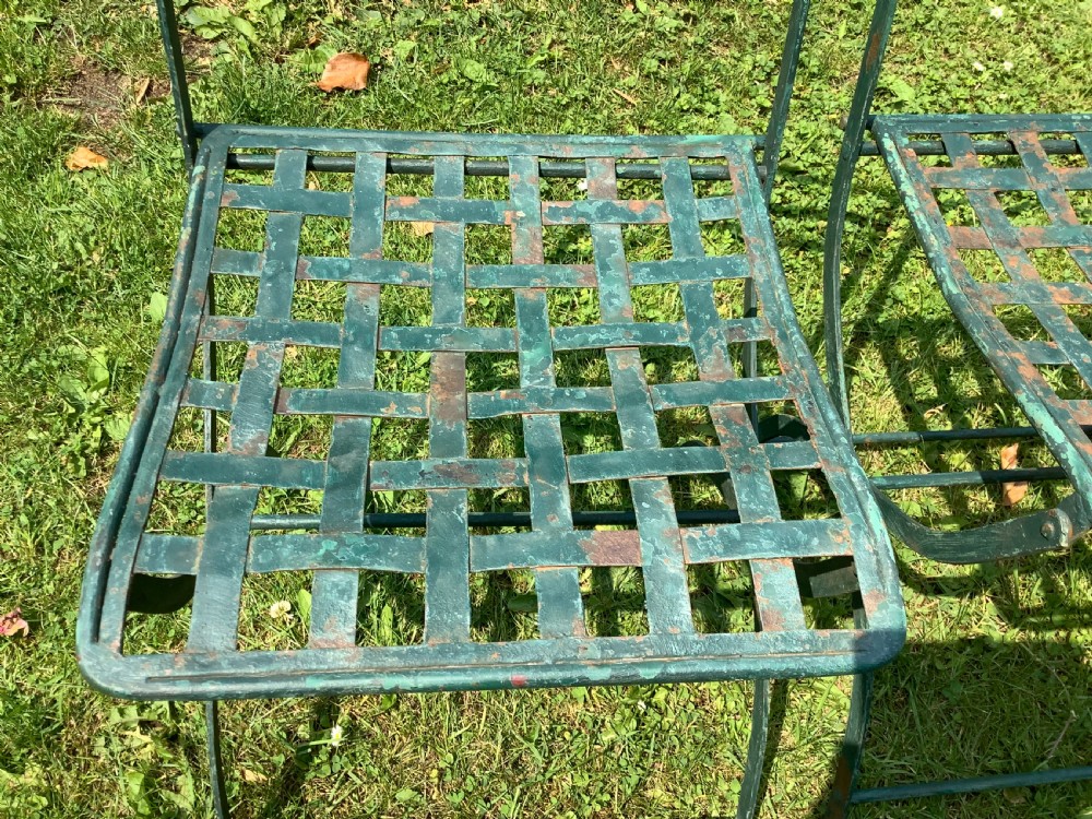 A set of four weathered green painted French folding iron garden chairs with lattice strap seats resting on grass. View XI