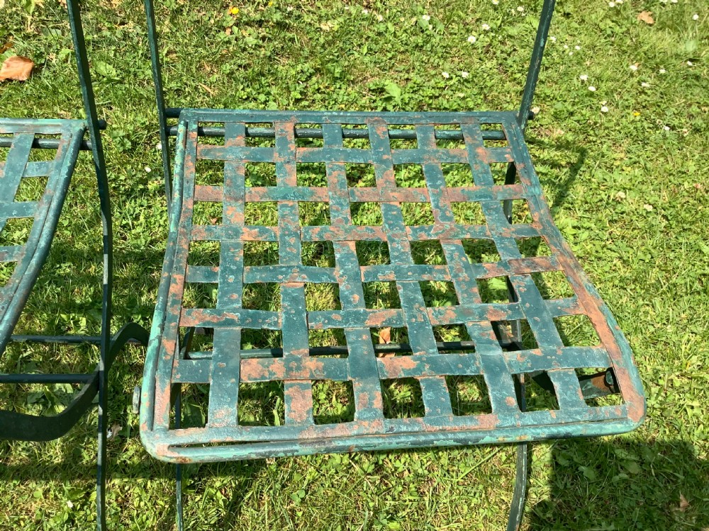 A set of four weathered green painted French folding iron garden chairs with lattice strap seats resting on grass. View XII