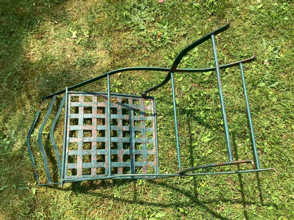 A set of four weathered green painted French folding iron garden chairs with lattice strap seats resting on grass. View XIII