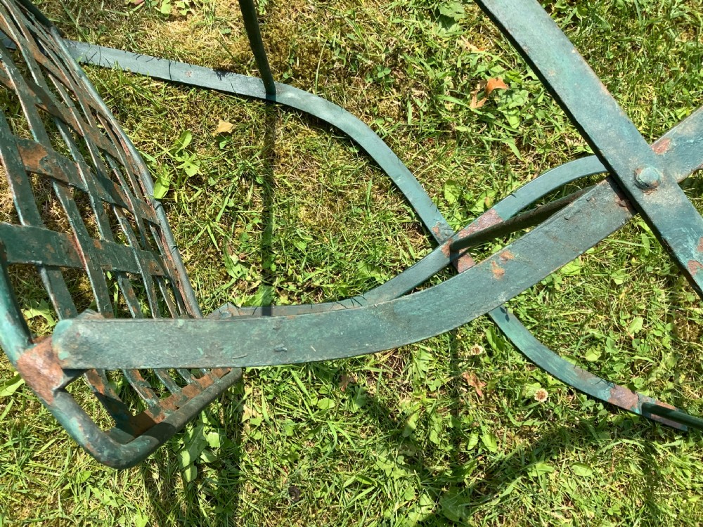 A set of four weathered green painted French folding iron garden chairs with lattice strap seats resting on grass. View XVI