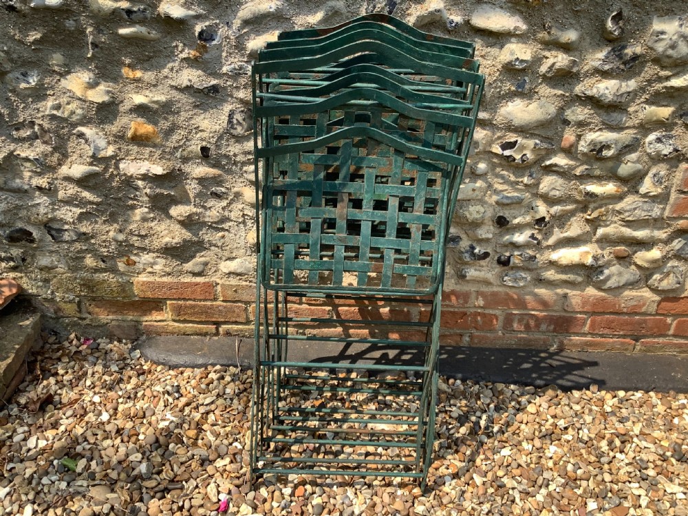 A set of four weathered green painted French folding iron garden chairs with lattice strap seats resting on grass. View XVII
