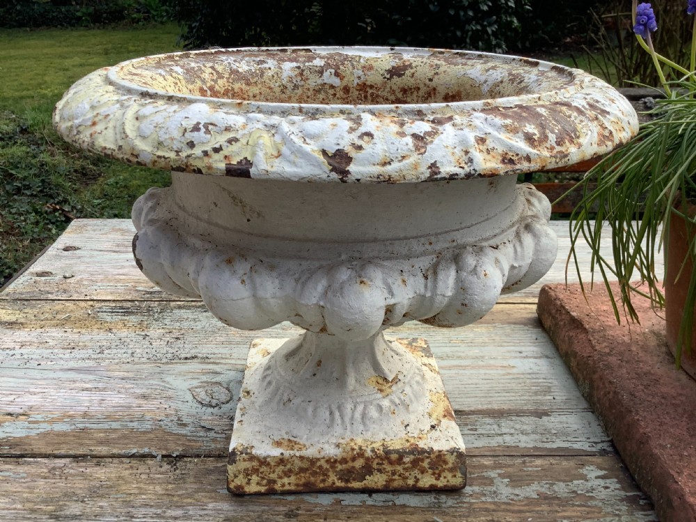 A pair of weathered off-white cast iron table urns featuring classical gadrooned decoration and square pedestal bases. View VI