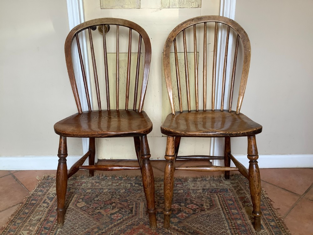 A near pair of antique wooden stick back Windsor kitchen chairs with hoop backs and turned legs.