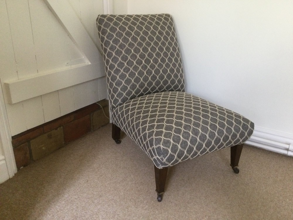 A 19th-century English low-seated slipper chair upholstered in grey patterned fabric with square tapered wooden legs on brass castors. View II