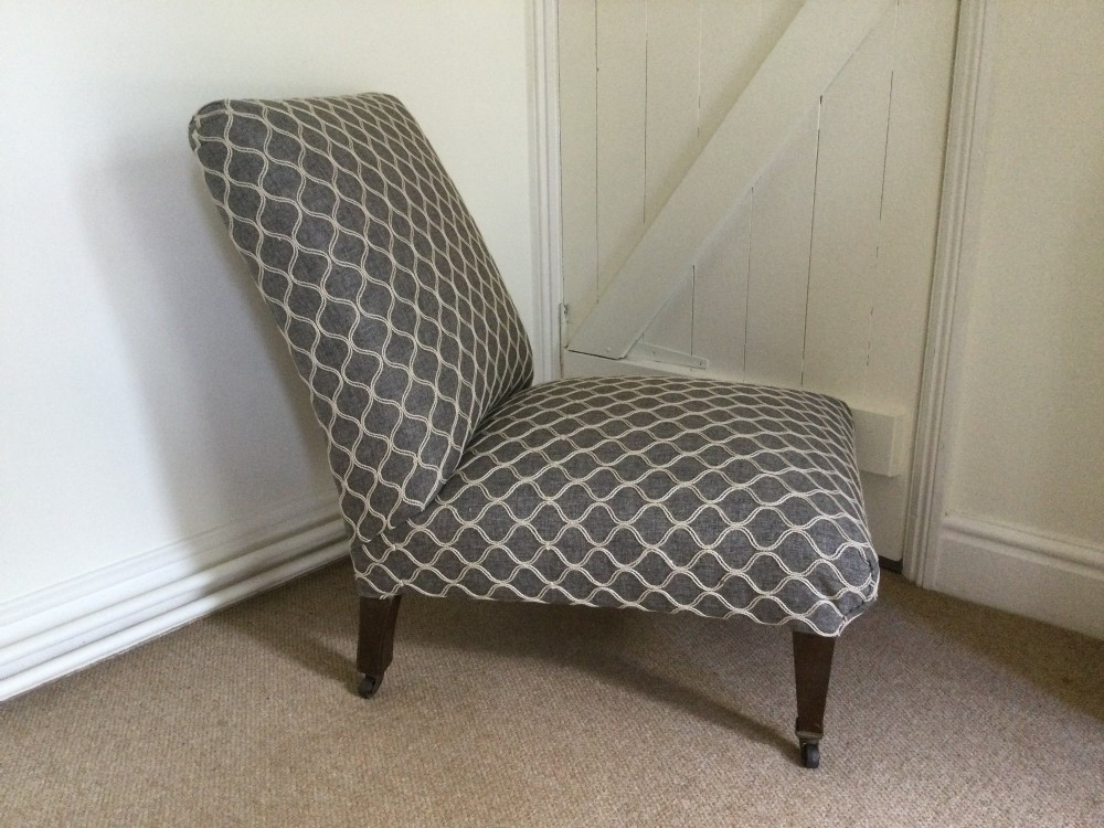 A 19th-century English low-seated slipper chair upholstered in grey patterned fabric with square tapered wooden legs on brass castors. View III