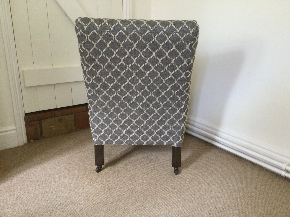 A 19th-century English low-seated slipper chair upholstered in grey patterned fabric with square tapered wooden legs on brass castors. View IV