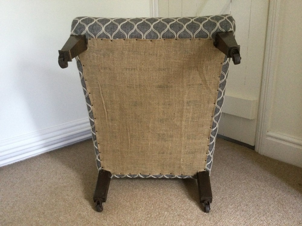 A 19th-century English low-seated slipper chair upholstered in grey patterned fabric with square tapered wooden legs on brass castors. View VII