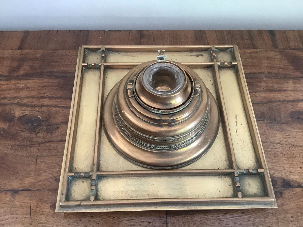 A square Victorian brass inkstand featuring a central domed hinged inkwell resting on a stepped base surrounded by pen channels. View II