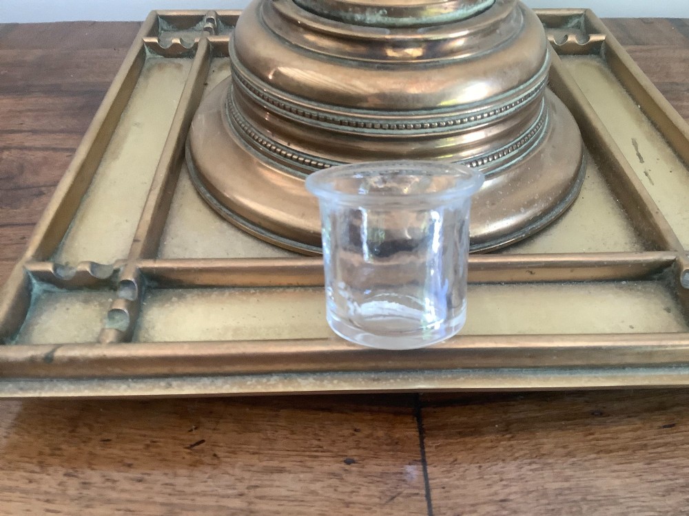 A square Victorian brass inkstand featuring a central domed hinged inkwell resting on a stepped base surrounded by pen channels. View IV