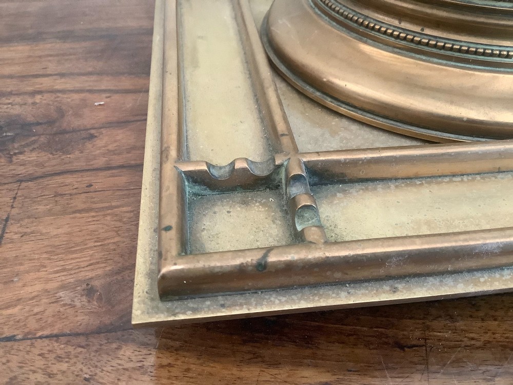 A square Victorian brass inkstand featuring a central domed hinged inkwell resting on a stepped base surrounded by pen channels. View IX