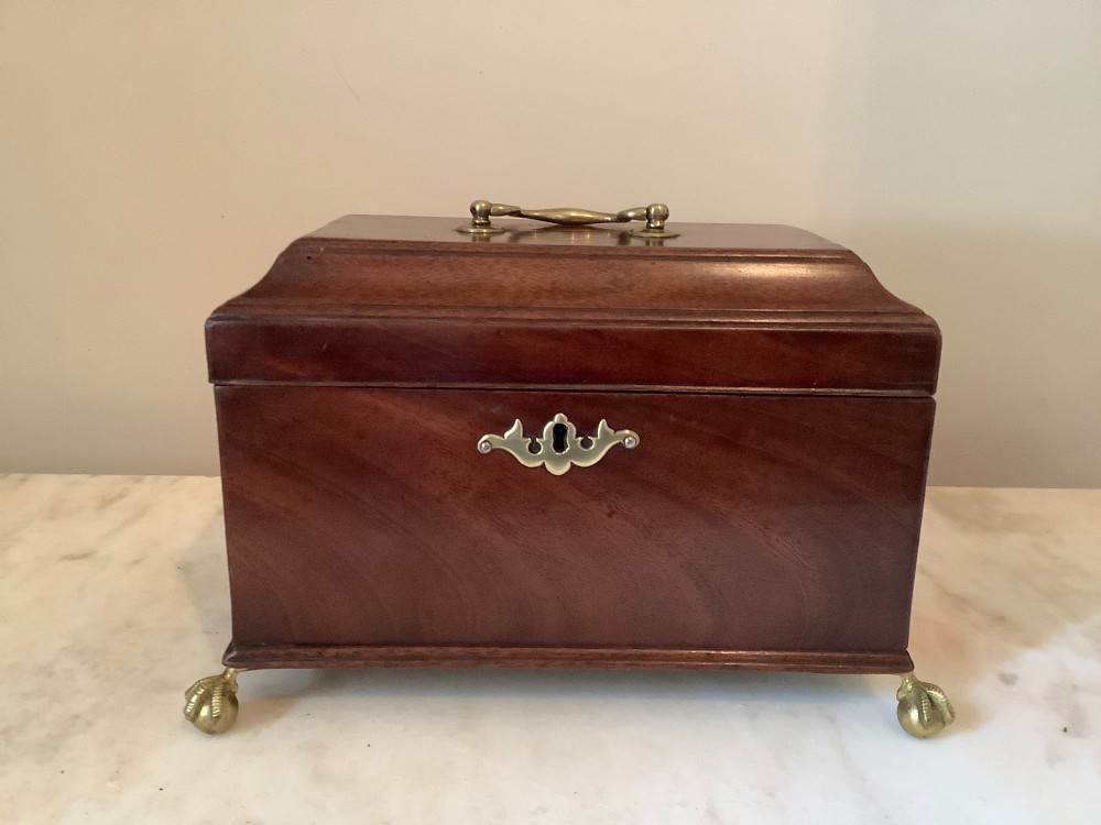 A Georgian mahogany tea caddy featuring brass ball-and-claw feet, a central brass escutcheon, and a top carrying handle.