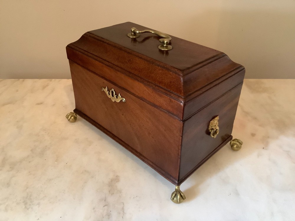 A Georgian mahogany tea caddy featuring brass ball-and-claw feet, a central brass escutcheon, and a top carrying handle. View II
