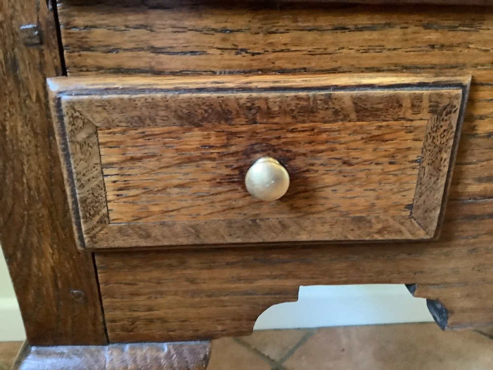 An 18th-century oak lowboy featuring a three-drawer configuration above an arched apron and cabriole legs ending in pad feet. View V