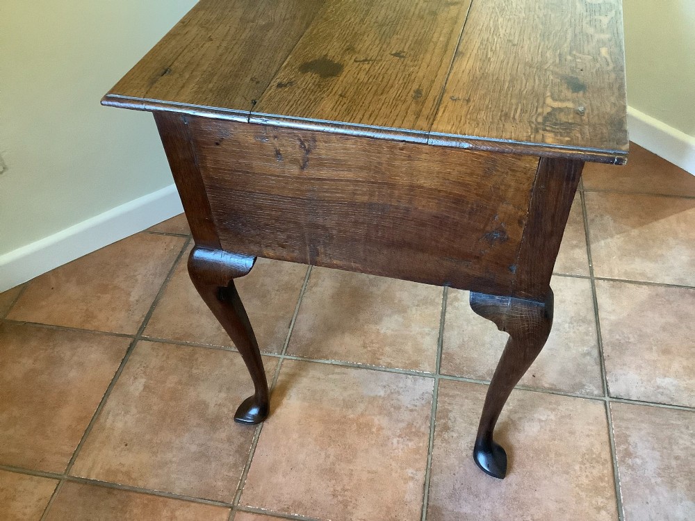 An 18th-century oak lowboy featuring a three-drawer configuration above an arched apron and cabriole legs ending in pad feet. View X