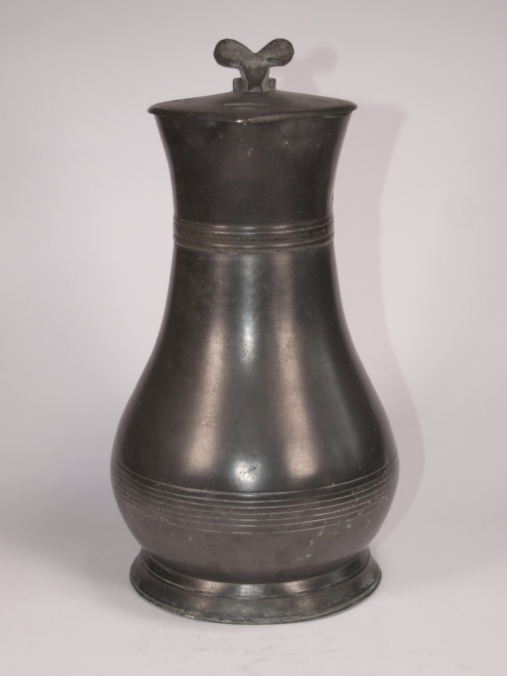 An antique dark grey pewter lidded flagon featuring a bulbous body, flared collar, hinged lid, and handle. View II