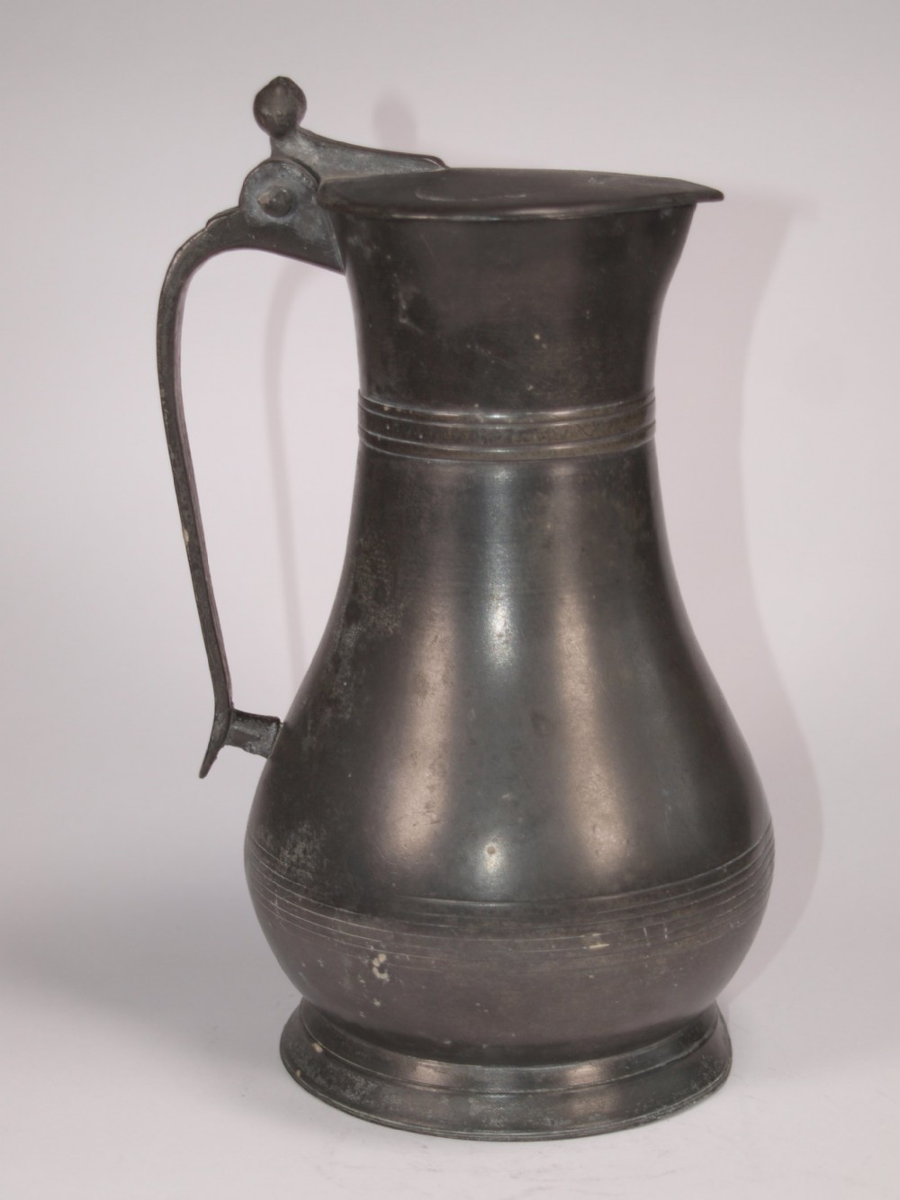 An antique dark grey pewter lidded flagon featuring a bulbous body, flared collar, hinged lid, and handle. View III